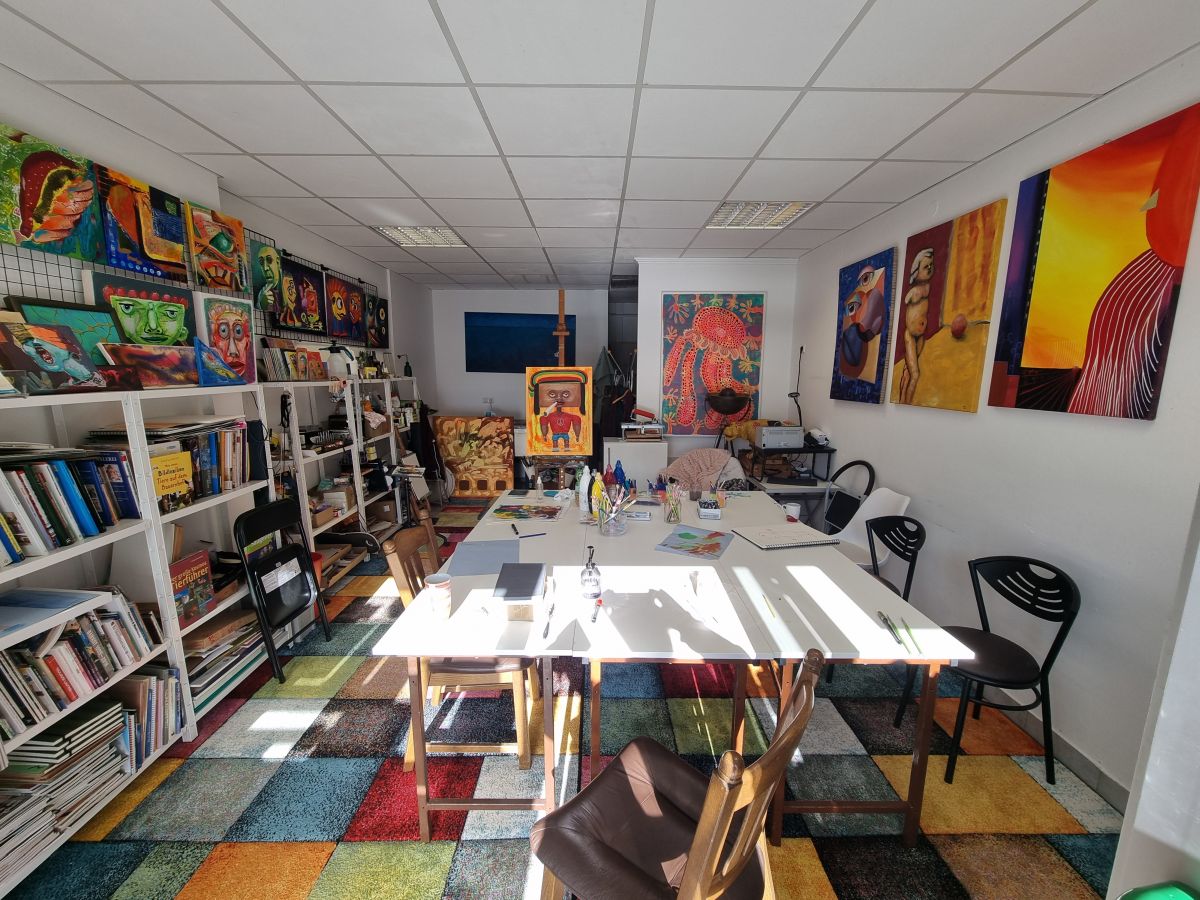 Foto vom Inneren des Künstlerateliers mit Tischen, Regalen, Büchern und Farben und natürlich einigen Werken an der Wand.